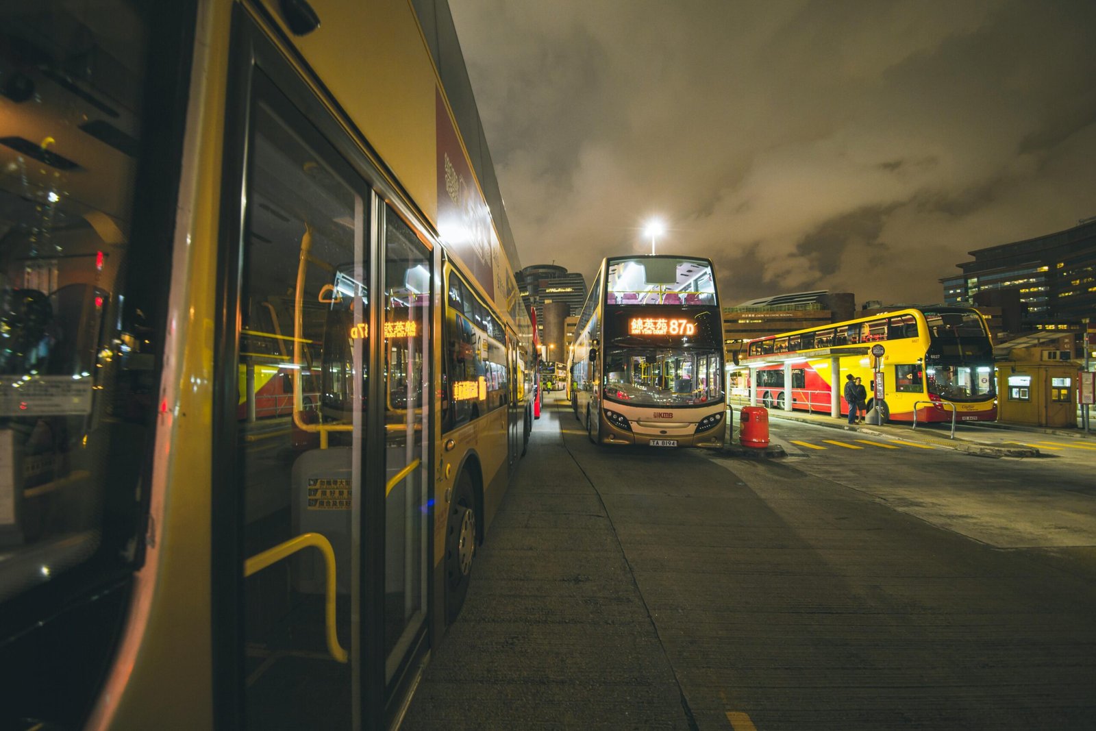 City buses at a bustling nighttime bus stop in Kowloon, showcasing urban public transportation.