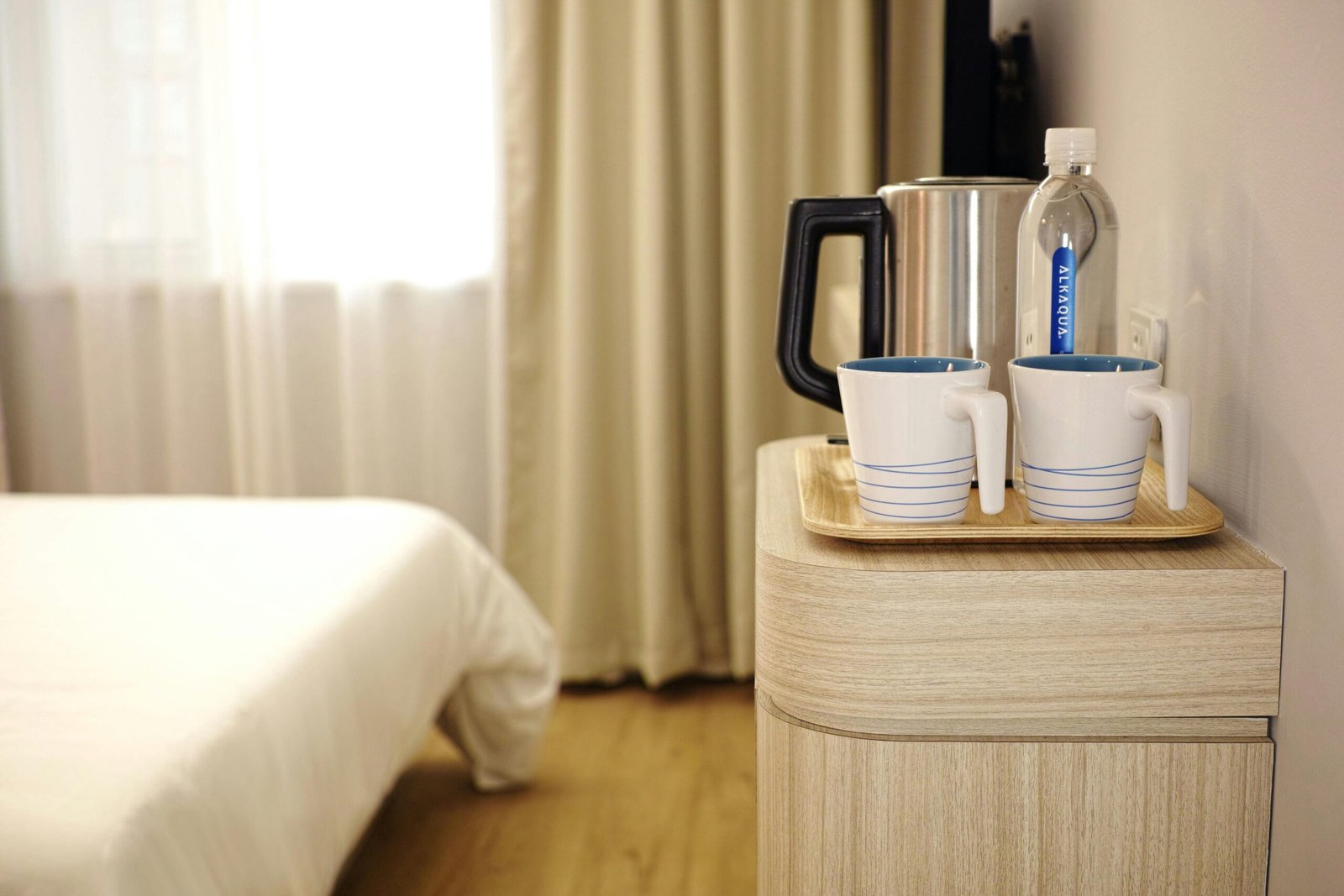Contemporary hotel room featuring a neatly arranged beverage setup on wooden furniture.